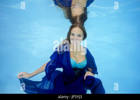 Frau im blauen Kleid posiert unter Wasser im pool Stockfoto