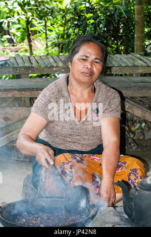 Ubud, Bali, Indonesien - 27. Juli 2013. Bäuerin auf dem Boden sitzend Rösten Kakao in traditionellen Platten Stockfoto