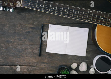 Schreibtisch des Komponisten des Songs für einen Arbeit Songwriter mit Gitarre und Notizblock auf Holztisch mit Vintage-Ton. Stockfoto