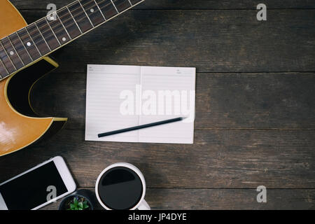 Schreibtisch des Komponisten des Songs für einen Arbeit Songwriter mit Gitarre und Notizblock auf Holztisch mit Vintage-Ton. Stockfoto