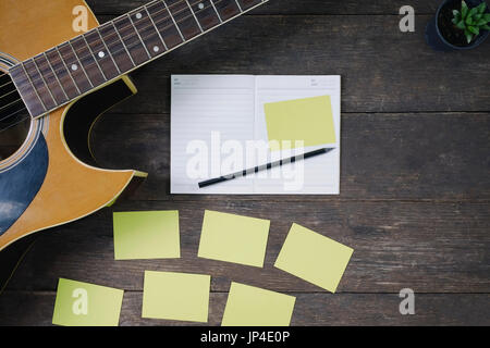 Schreibtisch des Komponisten des Songs für einen Arbeit Songwriter mit Gitarre und Notizblock auf Holztisch mit Vintage-Ton. Stockfoto