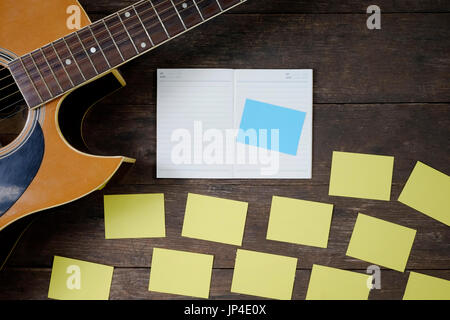 Schreibtisch des Komponisten des Songs für einen Arbeit Songwriter mit Gitarre und Notizblock auf Holztisch mit Vintage-Ton. Stockfoto