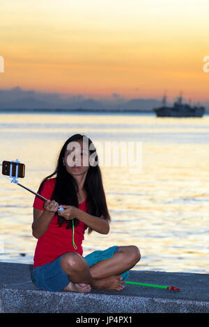 Mädchen nehmen selfie bei Sonnenuntergang in der Bucht von Manila, Roxas Boulevard, Philippinen Stockfoto