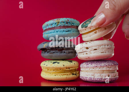 Viele Macarons. Roten Hintergrund. Weibliche Hand nimmt ein dessert Stockfoto