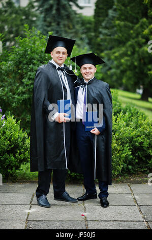 Zwei Absolventen der intelligent und gut aussehend in Graduierung Kleider und Mützen posiert mit ihrer Diplome. Stockfoto