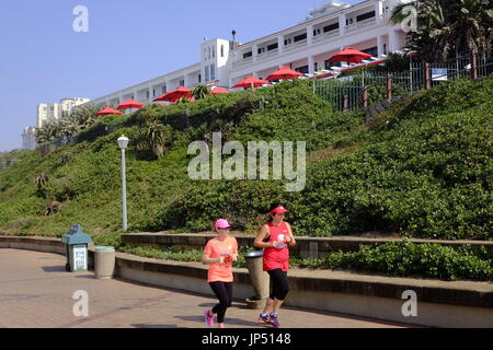 Umhlanga Rocks Durban in Südafrika. Jogger laufen entlang der Promenade direkt am Strand mit der Oyster Box Hotel im Hintergrund. Stockfoto