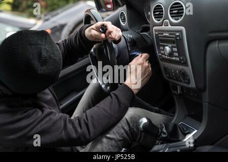 Mann gekleidet in schwarz mit einer Sturmhaube auf seinem Kopf versuchen, ein Auto zu laufen. Autodieb, Auto-Diebstahl-Konzept Stockfoto