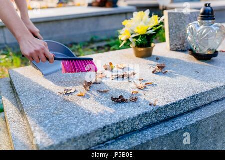 Eine Frau reinigt das Grab. Fegt Blätter aus dem Grabstein. Vorbereitungen für Allerheiligen am 1. November Stockfoto