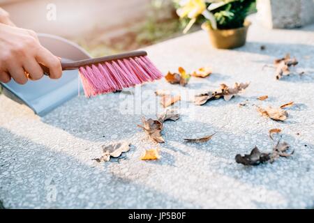 Eine Frau reinigt das Grab. Fegt Blätter aus dem Grabstein. Vorbereitungen für Allerheiligen am 1. November Stockfoto