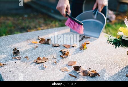 Eine Frau reinigt das Grab. Fegt Blätter aus dem Grabstein. Vorbereitungen für Allerheiligen am 1. November Stockfoto