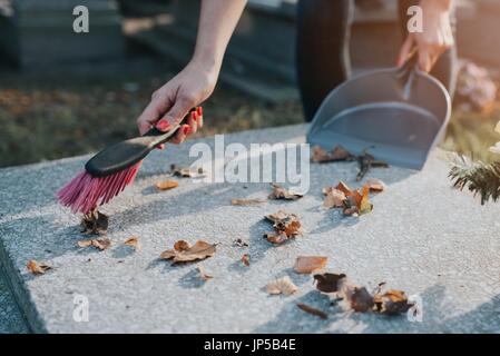 Eine Frau reinigt das Grab. Fegt Blätter aus dem Grabstein. Vorbereitungen für Allerheiligen am 1. November Stockfoto