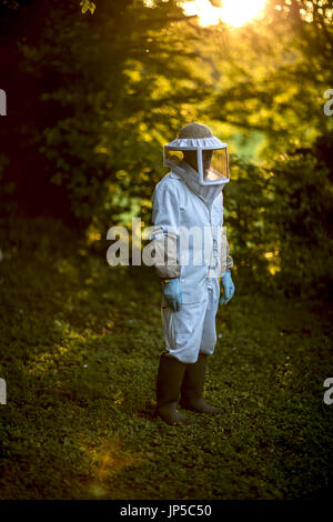 Imker trägt einen Schleier und Schutzkleidung in einem Wald. Stockfoto