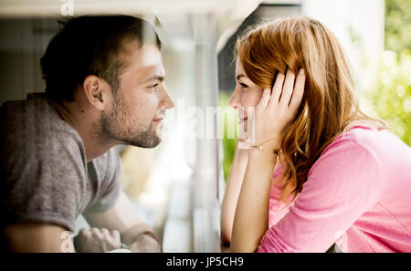 Ein paar lächelnd einander durch eine Glasscheibe eines Fensters. Stockfoto