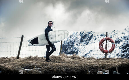 Ein Surfer tragen Anzüge tragen ein Surfbrett und wandern vorbei an einen Rettungsring. Stockfoto