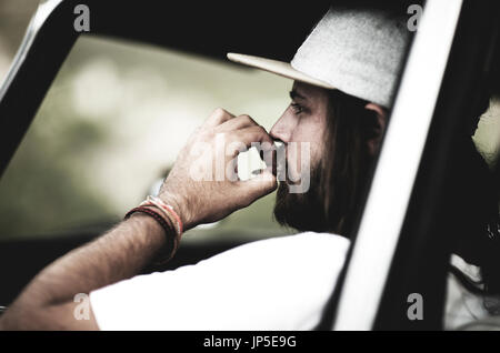 Bärtiger jungen Mann mit Baseballmütze in einem Auto sitzen Zigarette rauchen. Stockfoto