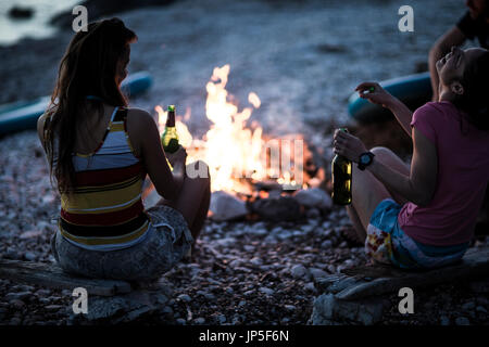 Eine Gruppe von jungen Leuten am Strand um ein Lagerfeuer versammelt... Stockfoto