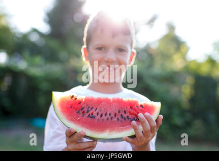 Kaukasische Kind Holding Stückchen Wassermelone in Outdoor-Sonnenuntergang Stockfoto