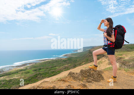 junge schöne weibliche Backpacker auf Berg Hügel mit Blick auf die Küstenlandschaft und Meeresbrise genießen, nachmittags Freizeit stehen. Stockfoto