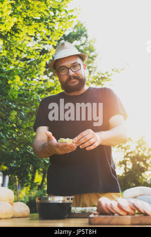 Hübsche Hipster Mann bereitet Fleisch und Zucchini-Burger, Bbq-Sommer-Garten Food-Konzept Stockfoto