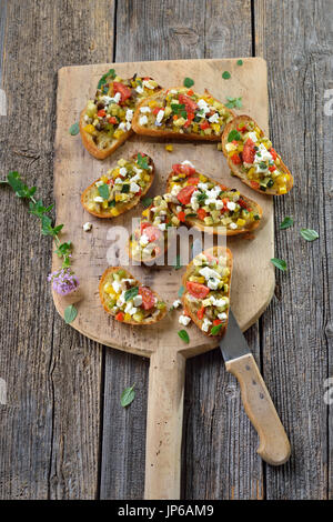 Vegetarische Häppchen zu wärmen: gebackene Crostini mit griechischen Mischgemüse mit Schafskäse serviert auf einem schäbigen Backen Board Stockfoto