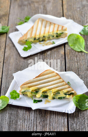 Vegetarische gedrückt doppelte Panini mit jungem Spinat Blätter, Zwiebeln und Käse serviert auf Pappteller auf einem Holztisch Stockfoto