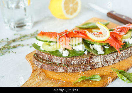 Sandwich mit geräuchertem Lachs, Gemüse und Quark auf einem Holzbrett. Stockfoto