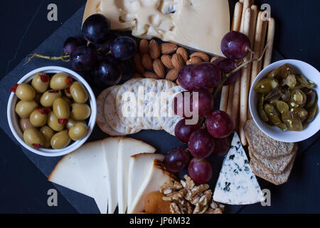 verschiedene Käse, Trauben, Crackern, Nüssen und Oliven auf einem schwarzen Hintergrund Stockfoto
