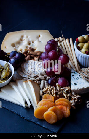 verschiedene Käse, Trauben, Crackern, Nüssen und Oliven auf einem schwarzen Hintergrund Stockfoto
