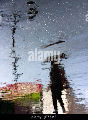 Verschwommen Person unter Dach Reflexion Schatten Silhouette auf regnerische Stadt Straße Asphalt Bürgersteig Stockfoto