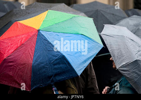 Horizontalen Blick auf einen bunten Regenschirm unter vielen schwarzen Schirmen im Regen. Stockfoto