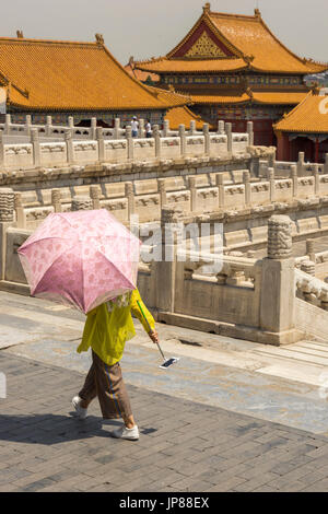 Frau mit Sonnenschirm Schatten und Handy mit Selfie Stock zu Fuß vom Palast der Himmlischen Reinheit in der verbotenen Stadt in Peking Stockfoto