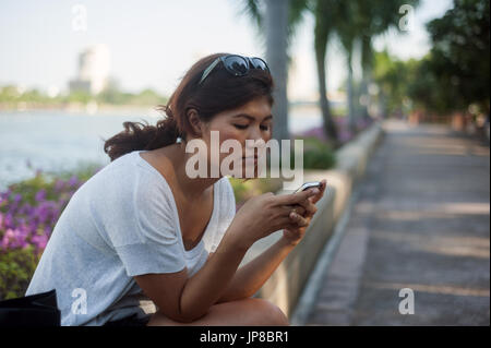 Junge Thai-Frau auf smartphone Stockfoto