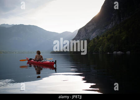 Frau in rot Kajak paddeln bei Sonnenuntergang auf See Bohinj, Slowenien. Stockfoto