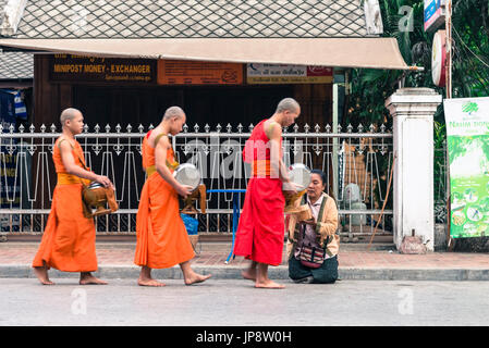 LUANG PRABANG, LAOS - MÄRZ 12, 2017: Lao Frau auf den Knien, die den Mönchen essen und Geld für die Buddhistische Almosen Preisverleihung, vor dem sunr Stockfoto