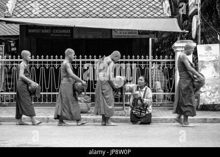 LUANG PRABANG, LAOS - MÄRZ 12, 2017: Schwarz/Weiß Bild von Lao Frau auf den Knien, die den Mönchen essen und Geld für die Buddhistische Almosen Givin Stockfoto