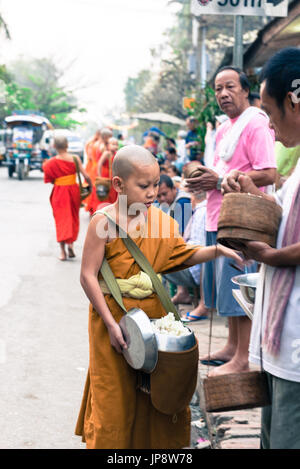 LUANG PRABANG, LAOS - MÄRZ 12, 2017: Vertikale Bild der junge Mönch empfangen foof Für die Buddhistische Almosen Preisverleihung, in Luang Prabang, Laos. Stockfoto