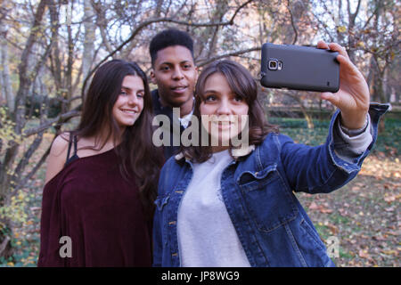 Gruppe von Jugendlichen, zwei kaukasische Mädchen und ein schwarzer Junge ein Selbstporträt im Feld mit einem Handy zu tun. Sie sind Freunde. Stockfoto