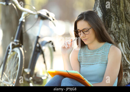 Einzelne Schüler tragen Brillen Auswendiglernen Noten sitzen in einem park Stockfoto