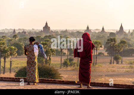 Eine burmesische Frau mit einem Mönch mit Blick auf die Pagdodas von Bagan, Pyathada Tempel in Bagan, Myanmar Stockfoto