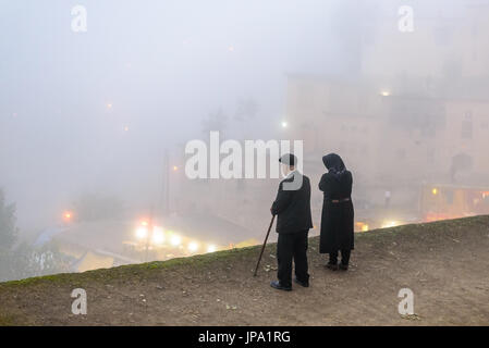 MASOULEH, IRAN - 5. Oktober 2014: Ältere paar am Rande des Daches, Blick über Bergdorf Masouleh im Nebel Stockfoto