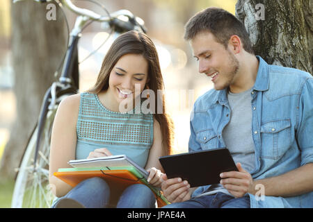 Zwei glückliche Schüler gemeinsam lernen online mit einem Tablet und Notizen in einem Park sitzt Stockfoto