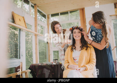 Alternative Hochzeit, Vorbereitung, Freunde schmücken Braut mit Blumenkranz Stockfoto