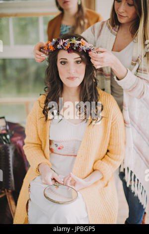 Alternative Hochzeit, Vorbereitung, Freundinnen schmücken Braut mit Blumenkranz Stockfoto