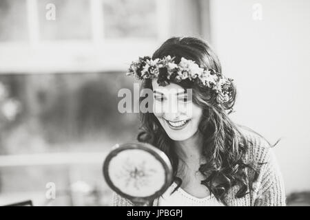 Alternative Hochzeit, Braut mit Blumenkranz schaut sich im Spiegel Stockfoto