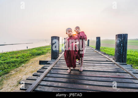 Amarapura, Mandalay Region, Myanmar. Mönche gehen auf die U Bein Brücke bei Sonnenaufgang. Stockfoto