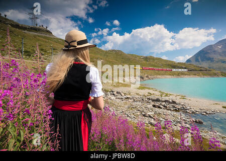 Frau mit traditionellen Kleidung bewundert die Roten Zug am Lago Bianco Berninapass Kanton Graubünden Engadin Schweiz Europa Stockfoto