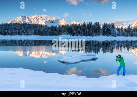 Fotograf in Aktion auf dem Ufer von Palù See wo schneebedeckte Berge und Wälder sind reflektiert Malenco Tal Lombardei Italien Europa Stockfoto