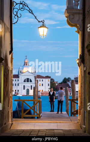 Touristen auf dem hölzernen Pier mit der Kirche gerahmt Le Zitelle im Hintergrund von den Lichtern der Dämmerung Venedig Veneto Italien Europa Stockfoto