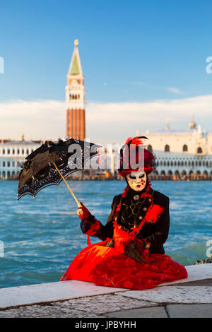 Porträt der Frau mit roten Kostüm und typische Maske des Karnevals von Venedig mit Markusplatz entfernt im Hintergrund Veneto Italien Europa Stockfoto