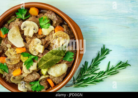 Ein Foto von einem Fleisch-Ragout in einer irdenen Schüssel mit Zweige frischer Rosmarin, geschossen von oben auf eine Hintergrundtextur blaugrün, mit einem Platz für text Stockfoto